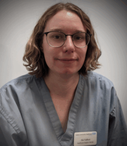 A person wearing a light blue medical scrub top with a name tag that reads 'Nia Talbot' and 'Medical Student.