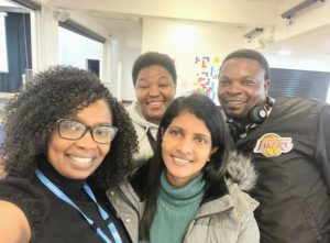 A group shot selfie photo of A group of four international nurses, wearing casual wear, all smiling at the camera.