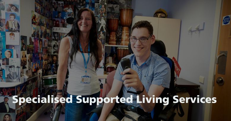 A young man in a wheelchair is smilling and holding a game controller. A support worker is stood behind them also smiling. Text: Specialised Supported Living Services