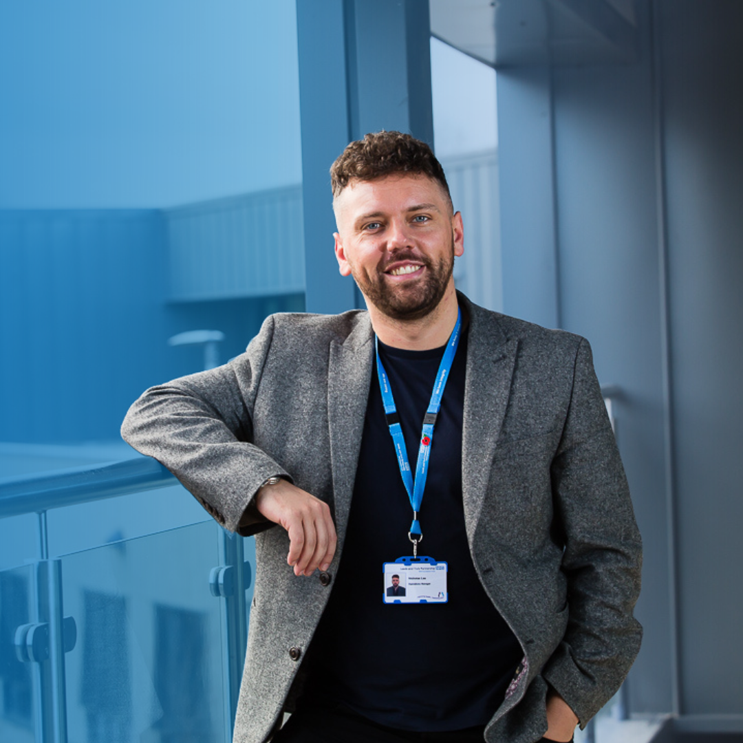 A man in a suit stands confidently in front of a wall, showcasing a professional appearance. There is a blue tint to the background. There is a link to a web page on this website.