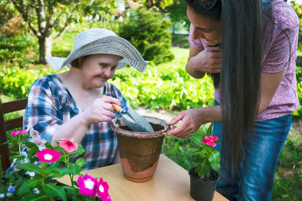 A woman pots a plant with help from another woman.
