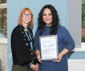 Two people pose with an award against a blue wall backdrop.