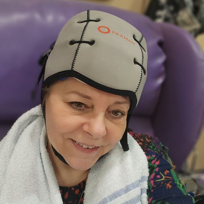 Person seated on a purple chair wearing a grey cap with a white towel around their shoulders.