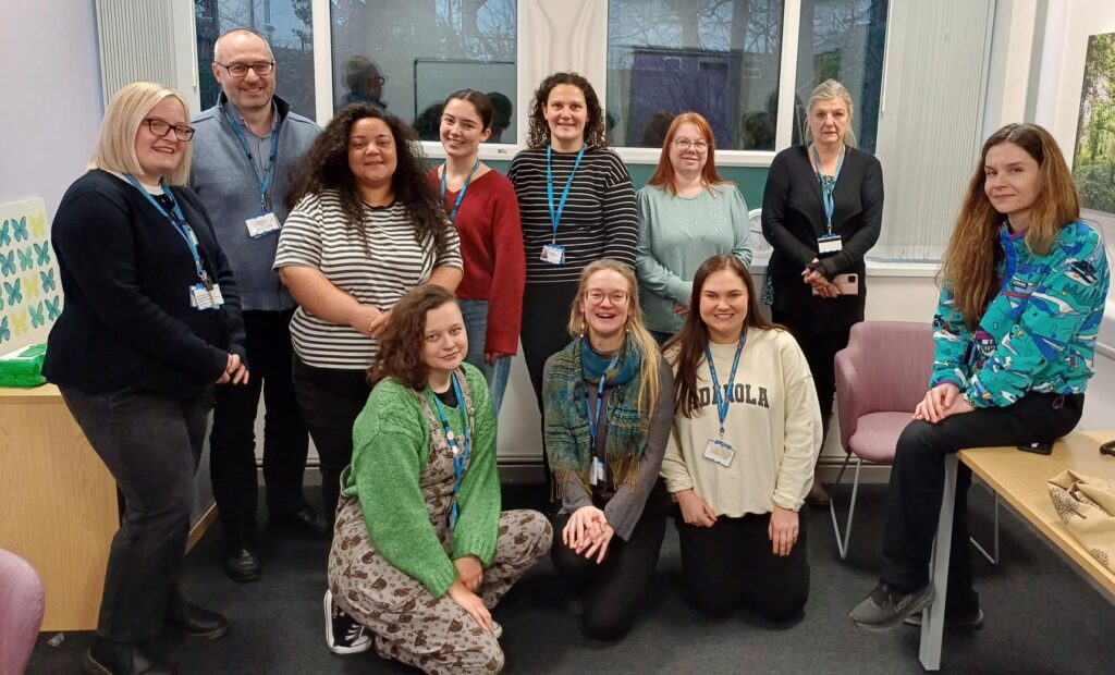 A photograph of a team of people sitting and standing as a group in a small office