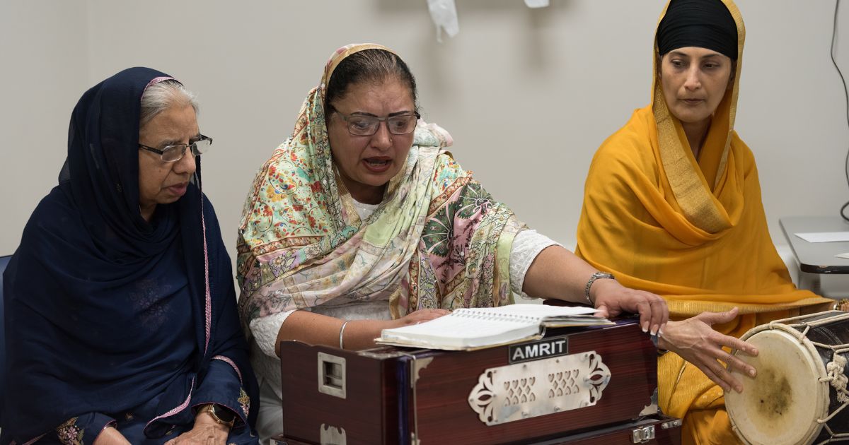 Three women dressed in traditional saris sit with a musical instruments, enjoying the Vaisakhi celebration.