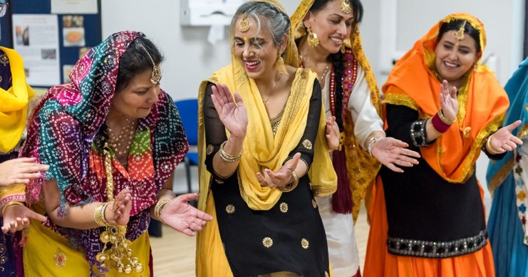 A group of women in traditional sikh clothing dance and clap.