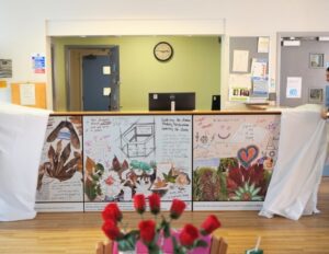 A reception desk decorated with colourful hand-drawn art and leaves is being unveiled in a bright, modern office space.