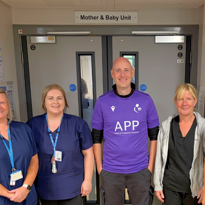Chris Wasley in a purple football shirt outside the door to the mother and baby unit alongside staff