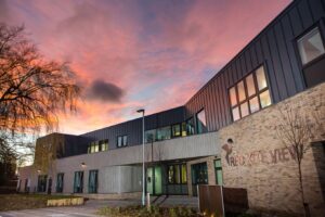 Exterior of the Red Kite View building at sunset, showing a modern two‑storey structure with large windows and a pink and orange sky in the background.
