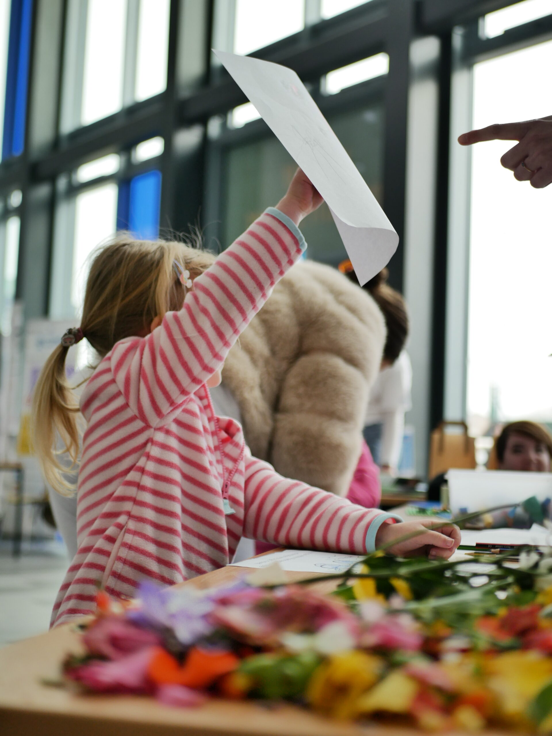 A young child wearing a red and white stripped top is holding a piece of paper in the air.