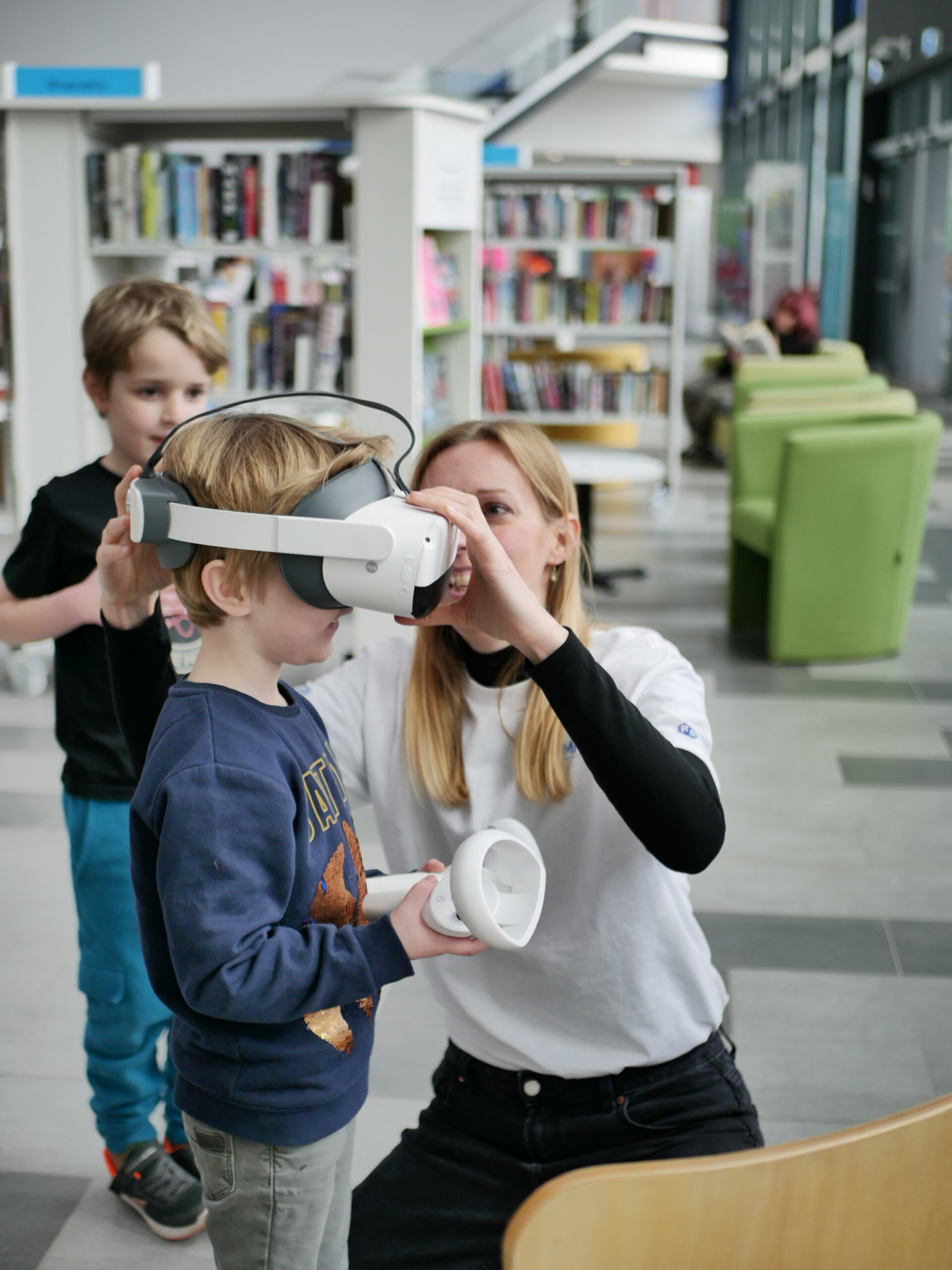 A woman is adjusting a virtual reality headset on a young child and another is watching in the background.