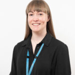 A medium close up of a young woman wearing a black shirt and blue lanyard.