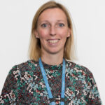 A person with light‑coloured, shoulder‑length hair is wearing a high‑neck, long‑sleeved top with a dense floral pattern in green, white, red and black. A blue LYPFT lanyard hangs around the person’s neck. The background is plain and white.