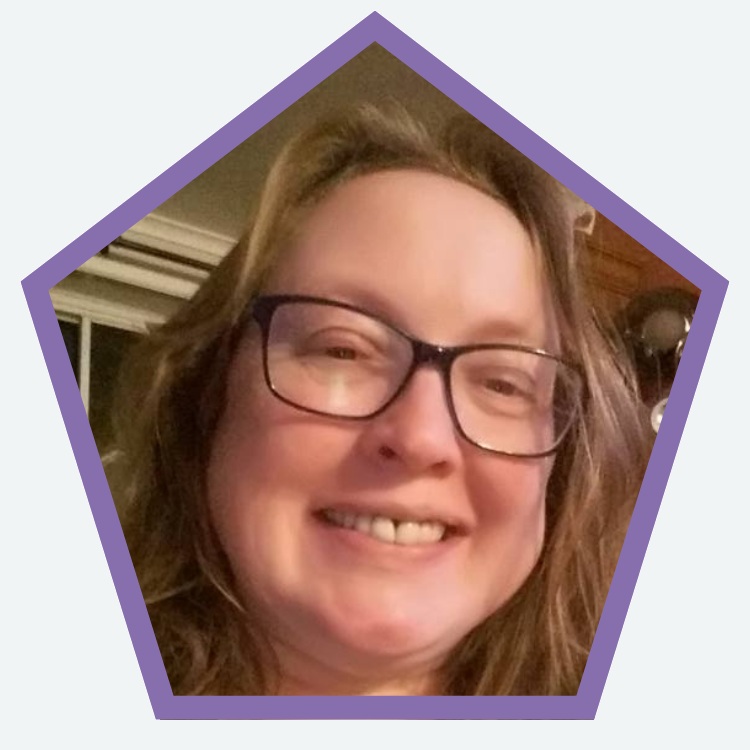 A close-up portrait inside a purple pentagon-shaped frame showing a person wearing rectangular glasses. The person has shoulder-length light brown hair and is smiling, facing the camera. The photo is taken indoors with a softly lit background that includes a window and wooden furniture.